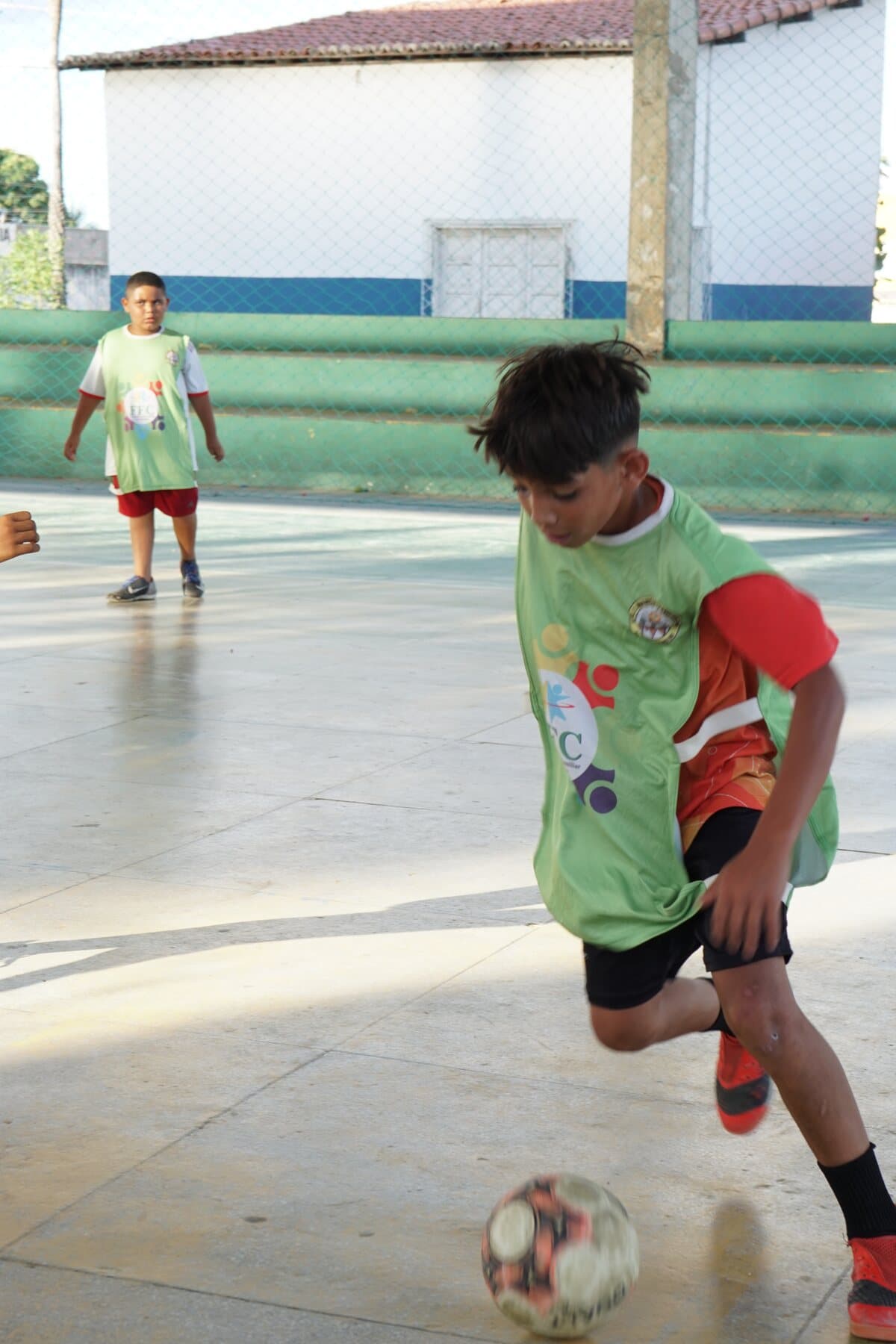 Criança com colete verde se movimenta durante uma atividade de futsal do FFC.