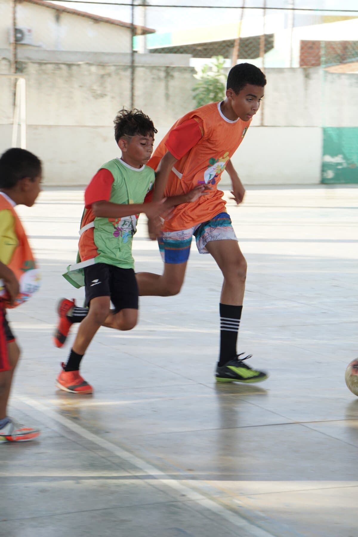 Crianças do FFC correm durante uma atividade de futsal na quadra.