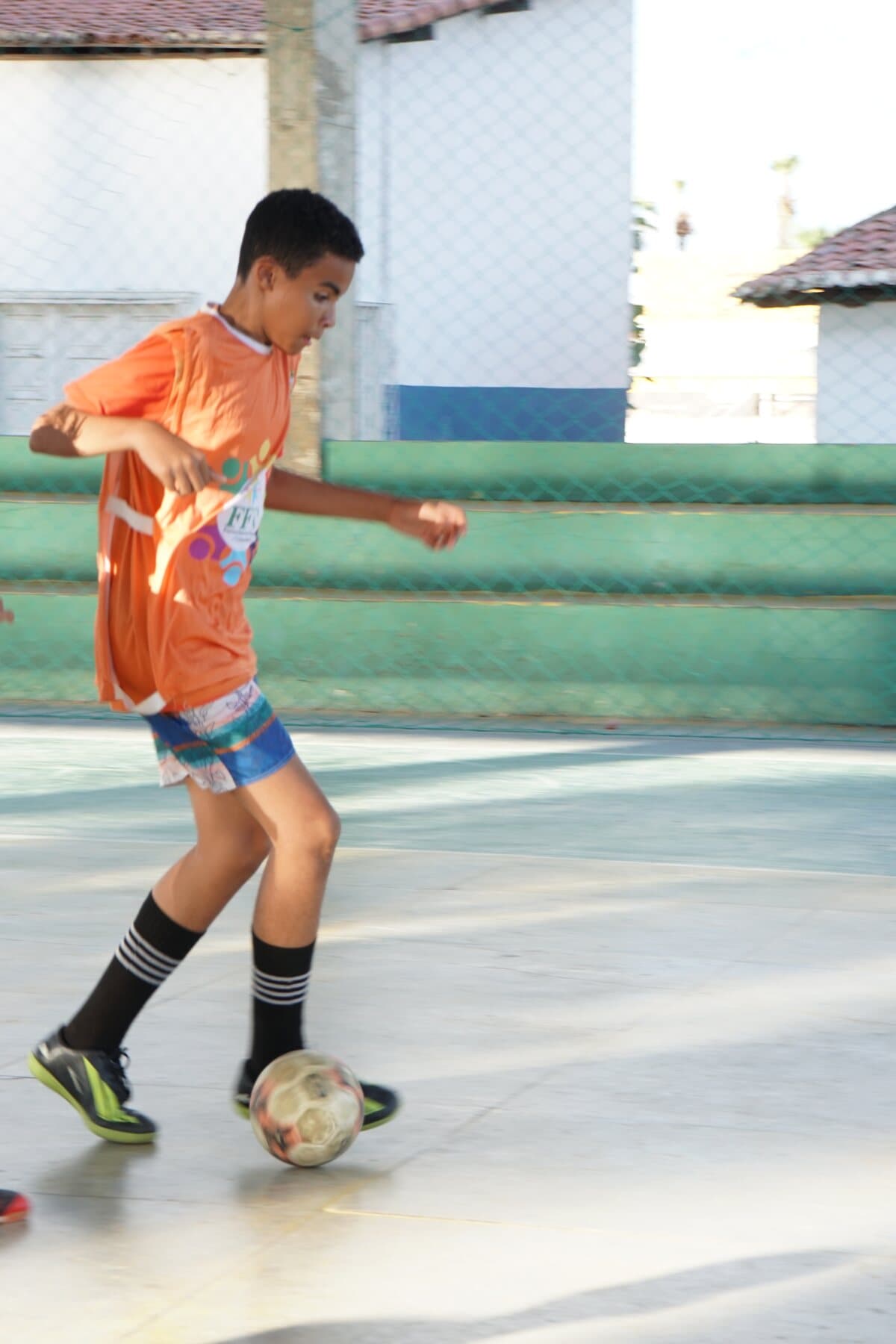 Criança de uniforme laranja corre durante uma atividade de futsal do FFC.
