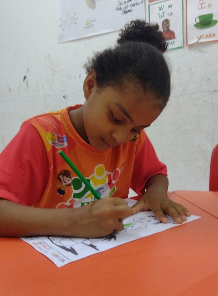 Menina do projeto FFC concentrada escrevendo em uma atividade pedagógica.