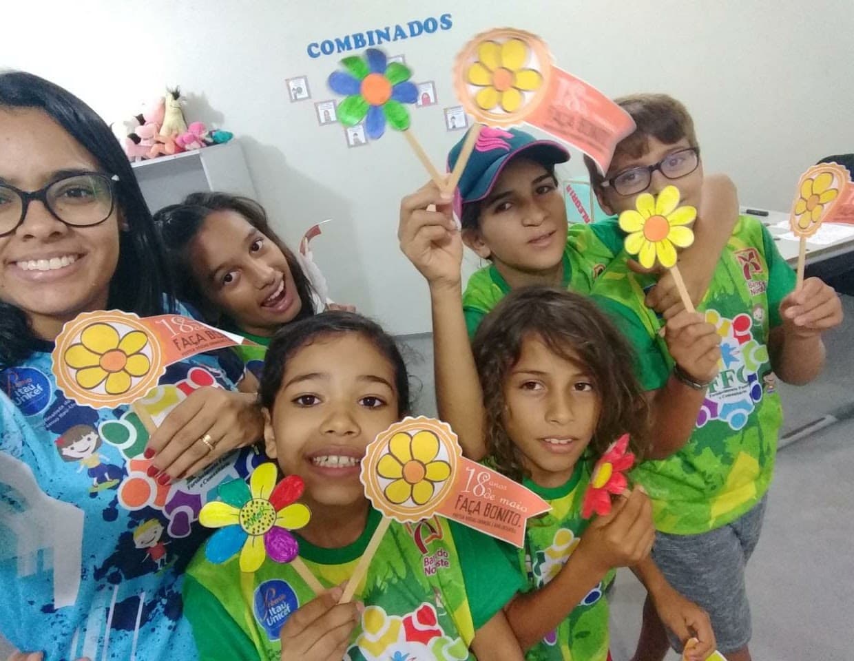 Educadora e crianças do FFC exibem flores de papel produzidas em oficina criativa.